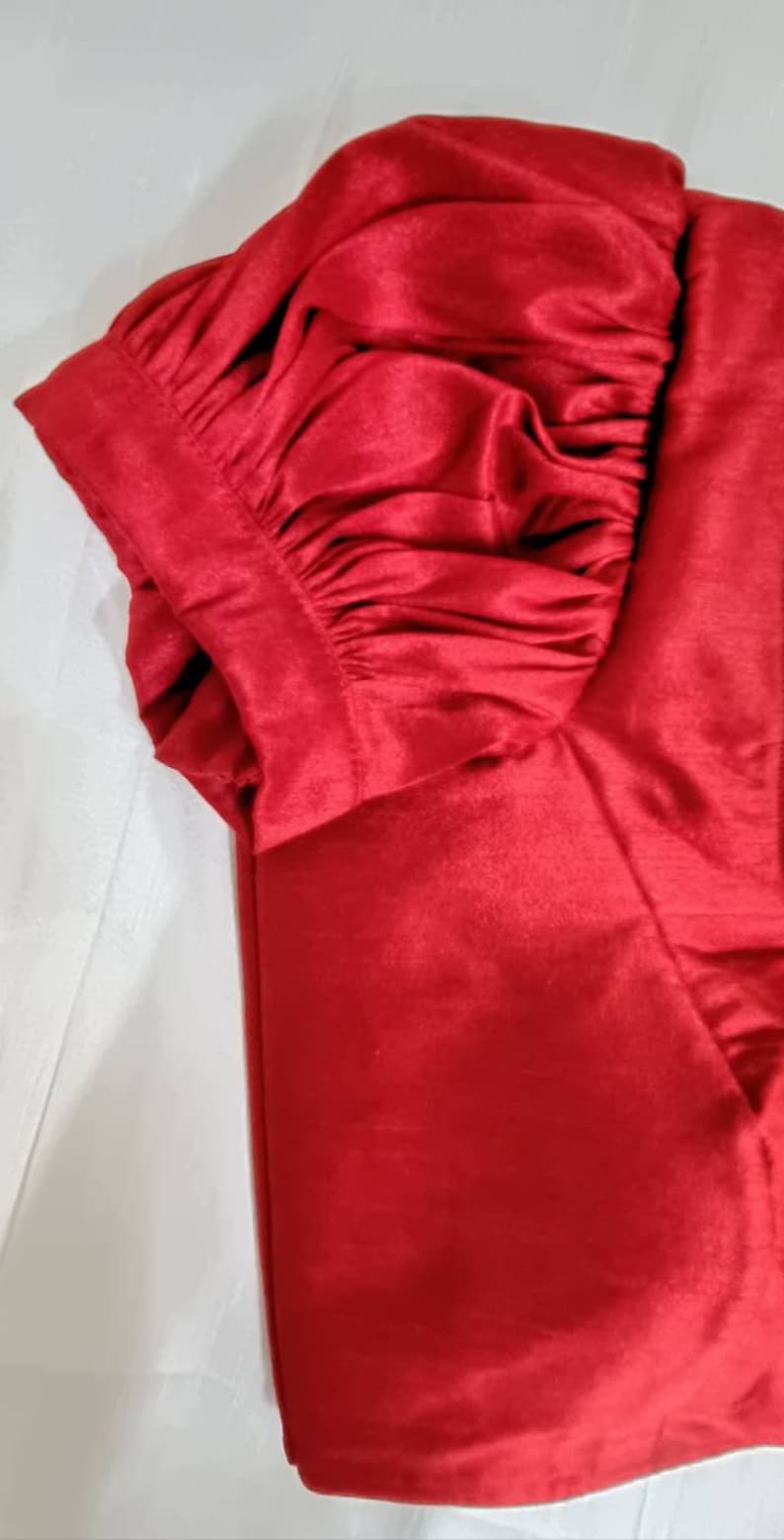 May include: A red satin fabric with a gathered, puffed sleeve detail. The fabric is smooth and shiny.