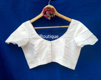 May include: White cotton blouse with a scoop neck and short, ruffled sleeves. The blouse is hanging on a wooden hanger.