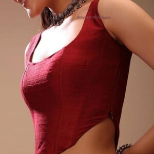 May include: A maroon sleeveless blouse with a square neckline and a zipper on the side. The blouse is made of a textured fabric.