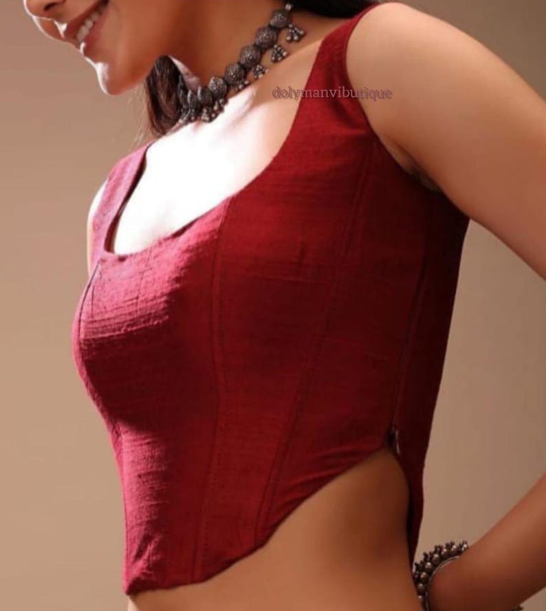 May include: A maroon sleeveless blouse with a square neckline and a zipper on the side. The blouse is made of a textured fabric.