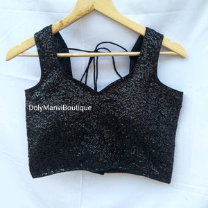 May include: A black sequined sleeveless top with a sweetheart neckline and a tie-up back. The top is on a wooden hanger.