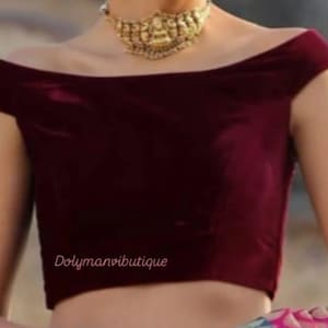 Op de afbeelding: Een maroon fluwelen top met off-shoulder en korte mouwen. De top is gecropped en heeft een aansluitende pasvorm. De tekst "Dolymanviboutique" is zichtbaar op de voorkant van de top.