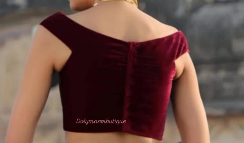 May include: A maroon velvet off-the-shoulder blouse with a gathered back detail. The blouse has short sleeves and a cropped length. The text "Dolymanviboutique" is visible at the bottom of the image.