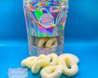 May include: A bag of freeze-dried fruit snacks called "Cosmic Crunch" with a holographic iridescent finish. The bag is open and several white, freeze-dried fruit rings are spilling out.