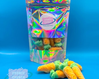 May include: A bag of freeze-dried carrot snacks from Cosmic Crunch. The bag is iridescent and has a pink logo with the text "Cosmic Crunch" and "Freeze Dried Treats". The carrots are orange and green and are arranged in a pile.