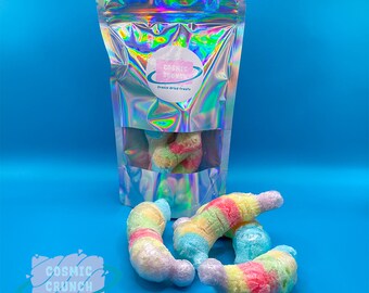 May include: A bag of freeze-dried treats called "Cosmic Crunch" with a rainbow swirl design. The bag is iridescent and has a clear window showing the treats inside. There are also four rainbow swirl freeze-dried treats outside of the bag.