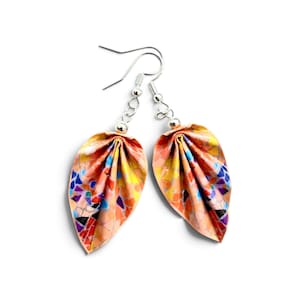 May include: A pair of drop earrings featuring leaf-shaped pendants with a multi-colored mosaic pattern in shades of orange, yellow, blue, and purple. The pendants are suspended from silver-toned metal hooks with small spherical accents.