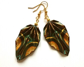 May include: A pair of dangling earrings featuring folded leaf-shaped pendants. The pendants display a dark pattern with orange, teal, and gold circular motifs. Each earring hangs from a gold-toned metal hook with a small gold bead accent.