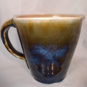 May include: A brown and blue ceramic mixing bowl with a handle. The bowl has a light brown glaze on the top and a dark blue glaze on the bottom.