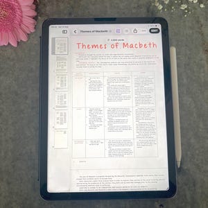 May include: A tablet displaying a digital document titled Themes of Macbeth, featuring a structured table with columns for theme, analysis, and context, alongside a white stylus pen resting on the side of the device screen.