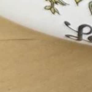 May include: White ceramic skillet with a white handle and a floral design featuring tomatoes, mushrooms, and herbs. The skillet has the text "Le Creuset" on the bottom.