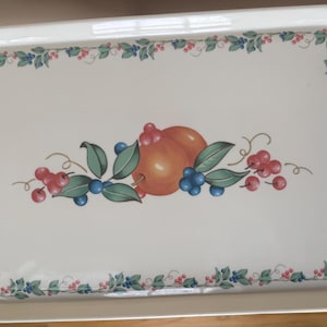 May include: Rectangular white serving tray with integrated handles. The tray features a decorative border of green leaves, blue berries, and red berries. The center design includes two orange fruits, green leaves, and more berries.