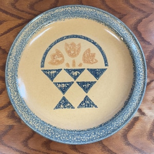 May include: A ceramic dinner plate with a blue and white rim and a tan center. The center features a blue and white design of a basket with three orange tulips.