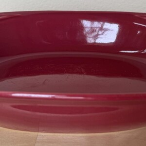 May include: A deep red ceramic baking dish with a scalloped rim and a textured design. The dish is empty and ready to be used for baking.