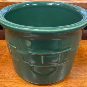 May include: A dark green ceramic planter with a basket weave design around the exterior. The planter has a rounded rim and a slightly tapered shape. The interior is a glossy dark green.