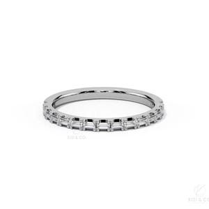 May include: A silver-toned band ring featuring a continuous row of small, rectangular baguette-cut clear stones set horizontally around the entire circumference. The metal band has a polished finish and the text KIZI & CO. is visible in the corner.
