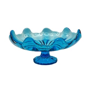 May include: A blue glass pedestal bowl with a wavy rim. The bowl is on a white background.