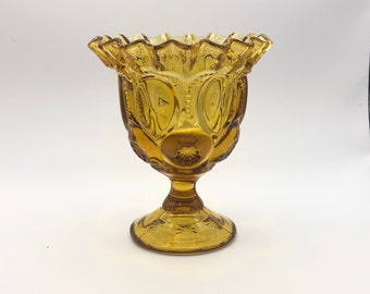 May include: A vintage amber glass pedestal bowl with a scalloped rim and a textured design. The bowl has a footed base.