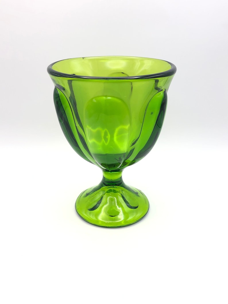 May include: A green glass goblet with a fluted design and a round base.