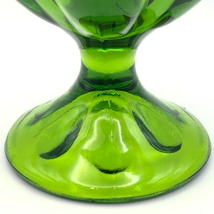 May include: A green glass bowl with a wide, flared rim and a pedestal base. The bowl has a smooth, shiny finish.