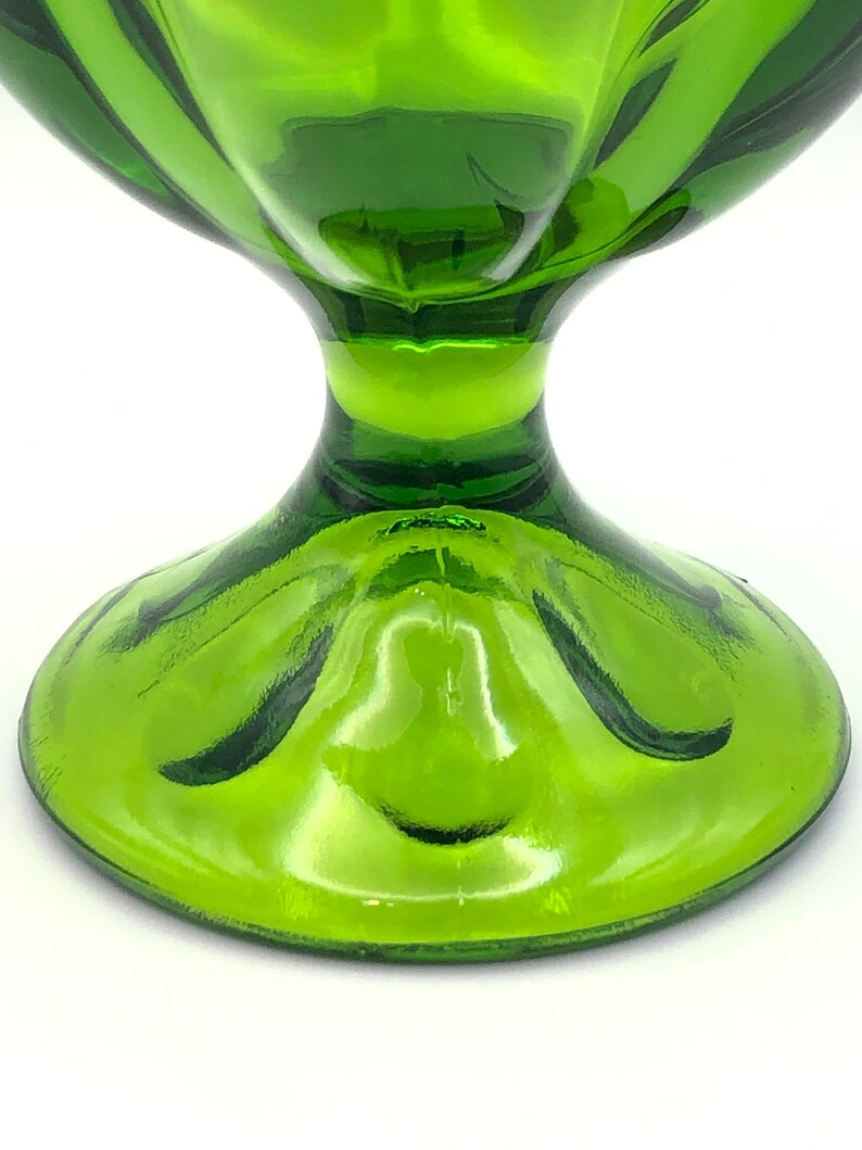 May include: A green glass bowl with a wide, flared rim and a pedestal base. The bowl has a smooth, shiny finish.