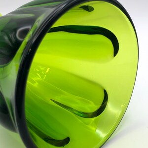 May include: A green glass vase with a unique, wavy design. The vase has a wide opening and a narrow base.