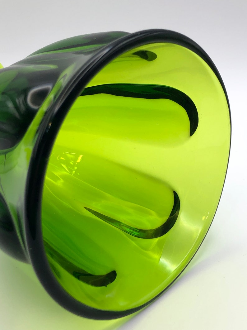 May include: A green glass vase with a unique, wavy design. The vase has a wide opening and a narrow base.