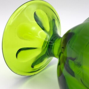 May include: A green glass goblet with a fluted base. The goblet is made of clear glass with a green tint.