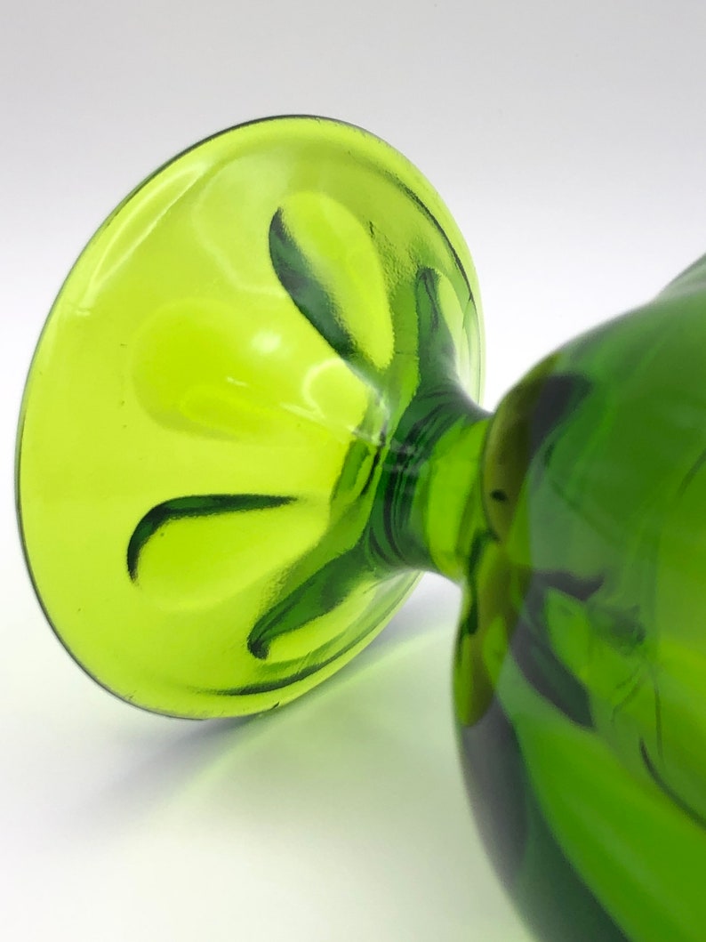 May include: A green glass goblet with a fluted base. The goblet is made of clear glass with a green tint.