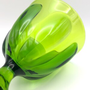May include: A green glass goblet with a unique, wavy design. The goblet is made of thick glass and has a wide, rounded bowl.
