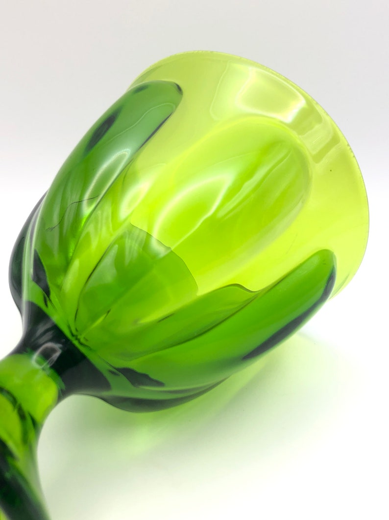 May include: A green glass goblet with a unique, wavy design. The goblet is made of thick glass and has a wide, rounded bowl.
