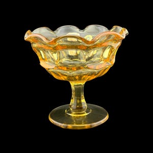 May include: A vintage yellow glass dessert bowl with a scalloped rim and a pedestal base. The bowl has a textured, geometric design and is likely from the mid-20th century. The bowl is approximately 5 inches in diameter and 4 inches tall.