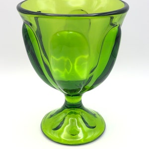 May include: A green glass pedestal bowl with a fluted design. The bowl has a wide, round base and a tall, slender stem.