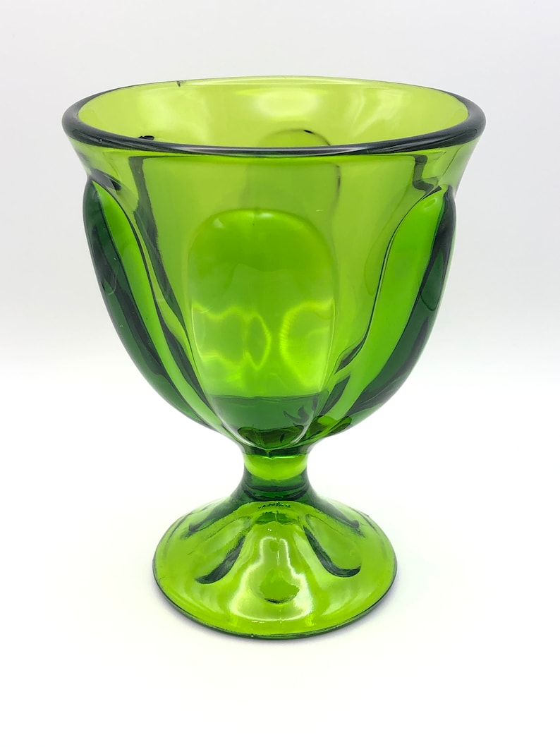 May include: A green glass pedestal bowl with a fluted design. The bowl has a wide, round base and a tall, slender stem.