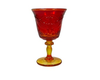 May include: A red glass goblet with a yellow stem and base. The goblet has a textured design of a bird with its wings spread.