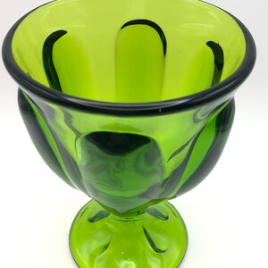 May include: A green glass goblet with a wide bowl and a short, thick stem. The bowl has a fluted design and the stem has a rounded base.