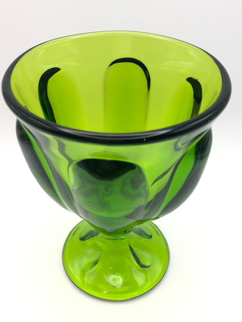 May include: A green glass goblet with a wide bowl and a short, thick stem. The bowl has a fluted design and the stem has a rounded base.