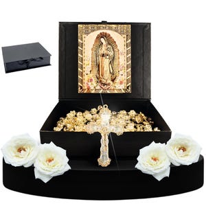 May include: A black velvet box with a gold-colored rosary inside. The rosary is in a black box with a picture of the Virgin Mary on the lid. The box is sitting on a black velvet base with white roses.