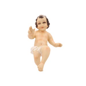May include: A white baby Jesus figurine with brown hair and a white diaper. The figurine is sitting with its right arm outstretched and its left hand resting on its leg.