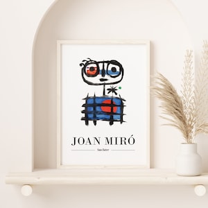 May include: A framed print of a colourful abstract painting by Joan Miró. The painting features a stylised figure with a red and blue face, a black grid pattern, and a red circle. The print is titled "Joan Miró - Sun Eater".