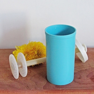 Puede incluir: Un vaso de plástico azul claro con un batidor de plástico blanco y una flor amarilla sobre una superficie de madera.