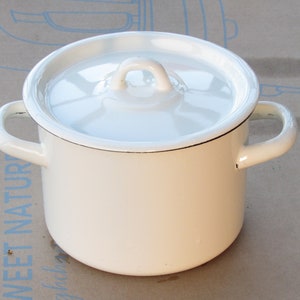 Op de afbeelding: Een witte emaille pan met een deksel en twee handvatten. De pan heeft een zwarte rand rond de bovenkant.