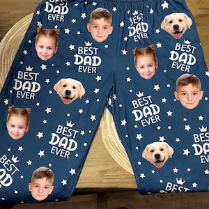 May include: Navy blue pajama pants with white stars, the phrase "BEST DAD EVER", and images of children and a golden retriever. The pajama pants have a drawstring waist and are made of a soft material.