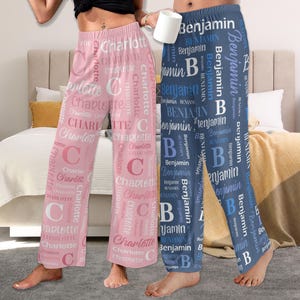 Puede incluir: Dos pares de pantalones de pijama con nombres impresos en ellos. Los pantalones de la izquierda son rosas con el nombre "Charlotte" impreso en blanco. Los pantalones de la derecha son azules con el nombre "Benjamin" impreso en blanco.