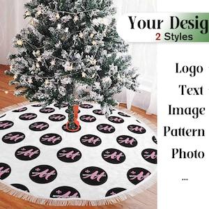 May include: White Christmas tree skirt with a black and pink pattern. The pattern features the text "My First Christmas" repeated throughout the skirt. The skirt has a fringe border.