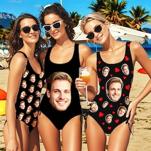 May include: Three women wearing black one-piece swimsuits with different patterns. One swimsuit features a repeated pattern of a man's face, another swimsuit features a repeated pattern of a man's face and red hearts, and the third swimsuit features a large image of a man's face.