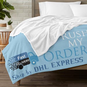 May include: A light blue blanket with the words "RUSH MY ORDER" and "Ship by DHL EXPRESS" printed in white and blue. A graphic of a delivery truck with the words "Fast DELIVERY" is also visible. A white blanket is draped over the blue blanket.