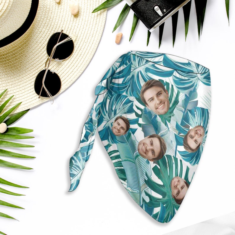 May include: A white bandana with a tropical leaf pattern and multiple faces printed on it. The bandana is tied in a knot at the top.