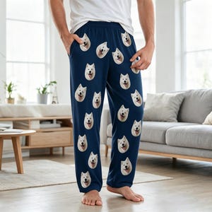 May include: Navy blue lounge trousers featuring a repeating pattern of white Samoyed dog faces. The trousers have an elastic waistband and side pockets, providing a relaxed fit for casual wear. The dog faces are evenly distributed across the fabric.