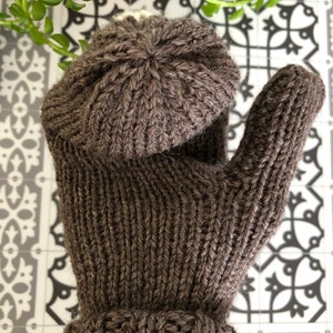 Pu&ograve; includere: Un cappello di lana marrone e guanti senza dita abbinati. Il cappello ha una trama a coste e i guanti hanno un motivo a treccia.